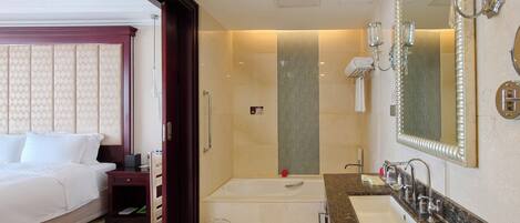 A hotel room with a large bed, a separate bathroom with a bathtub, a vanity with a mirror, and a shower area.