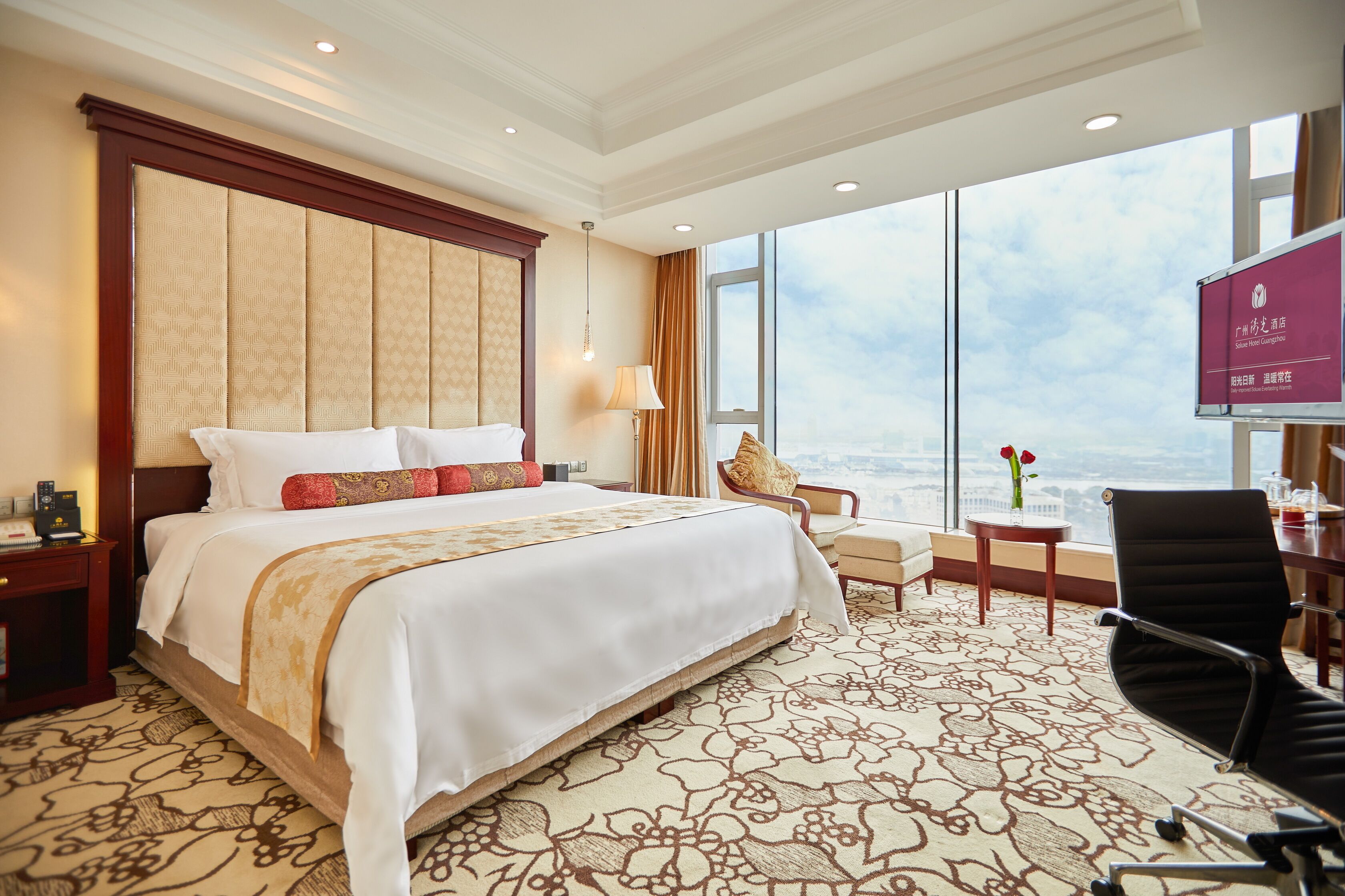 Ein Hotelzimmer mit einem großen Bett, einem Schreibtisch, einem Stuhl und Blick auf die Stadt.