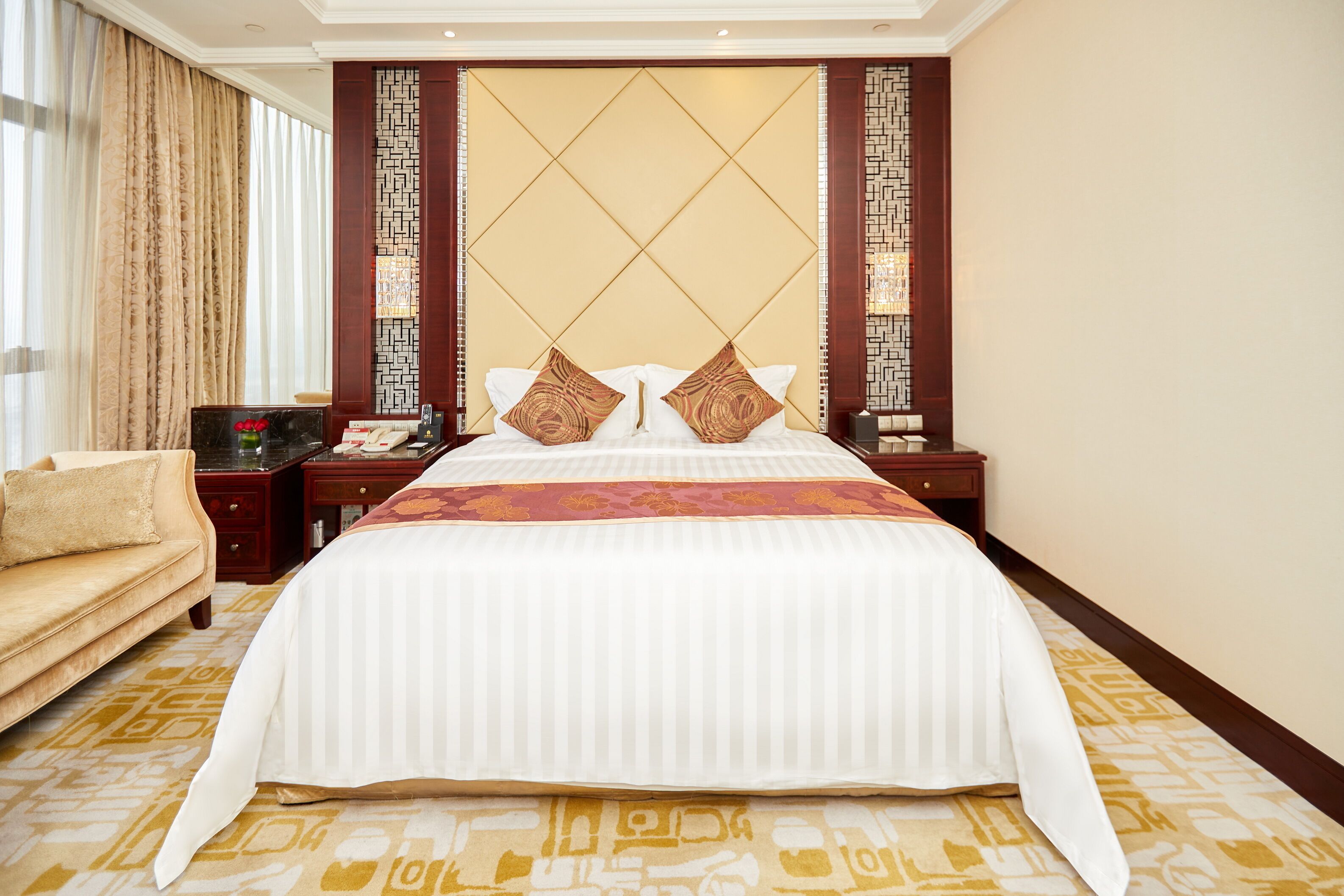 A hotel room with a large bed, a sofa, a nightstand, and a decorative wall panel.