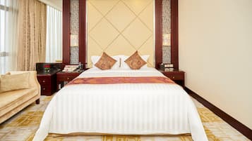 A hotel room with a large bed, a sofa, a nightstand, and a decorative wall panel.
