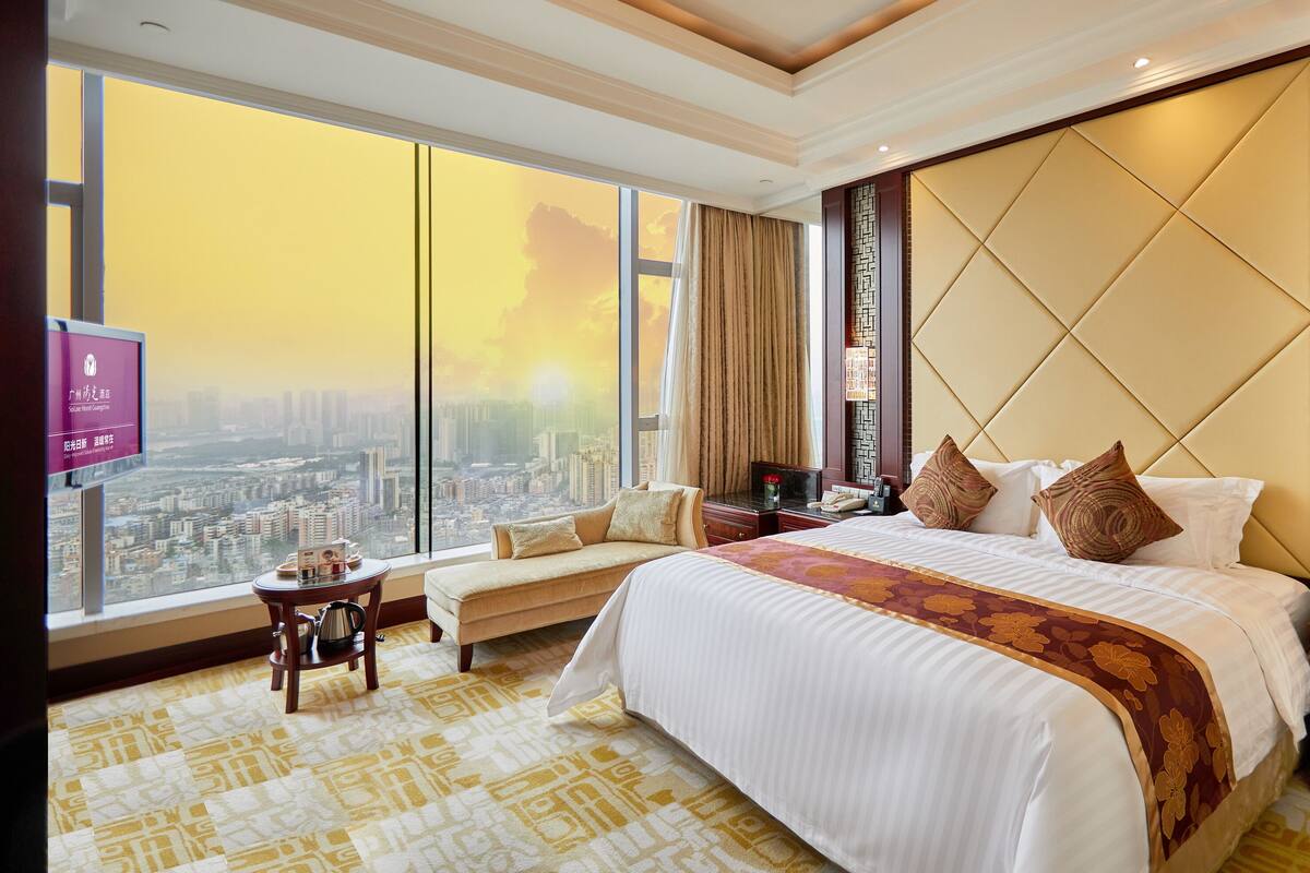 A hotel room with a large bed, a sofa, a small table with a coffee pot, and a TV on the wall.