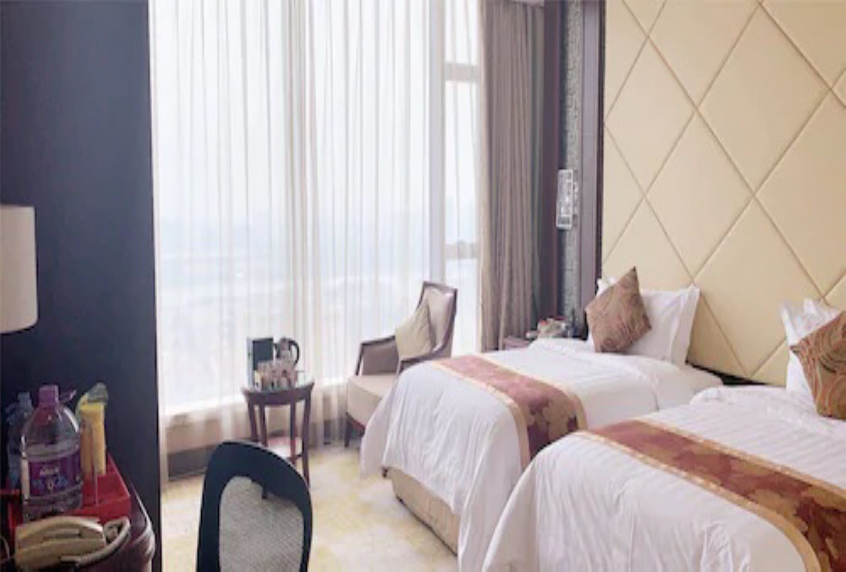A hotel room with two beds, a desk, a chair, and a window with curtains.
