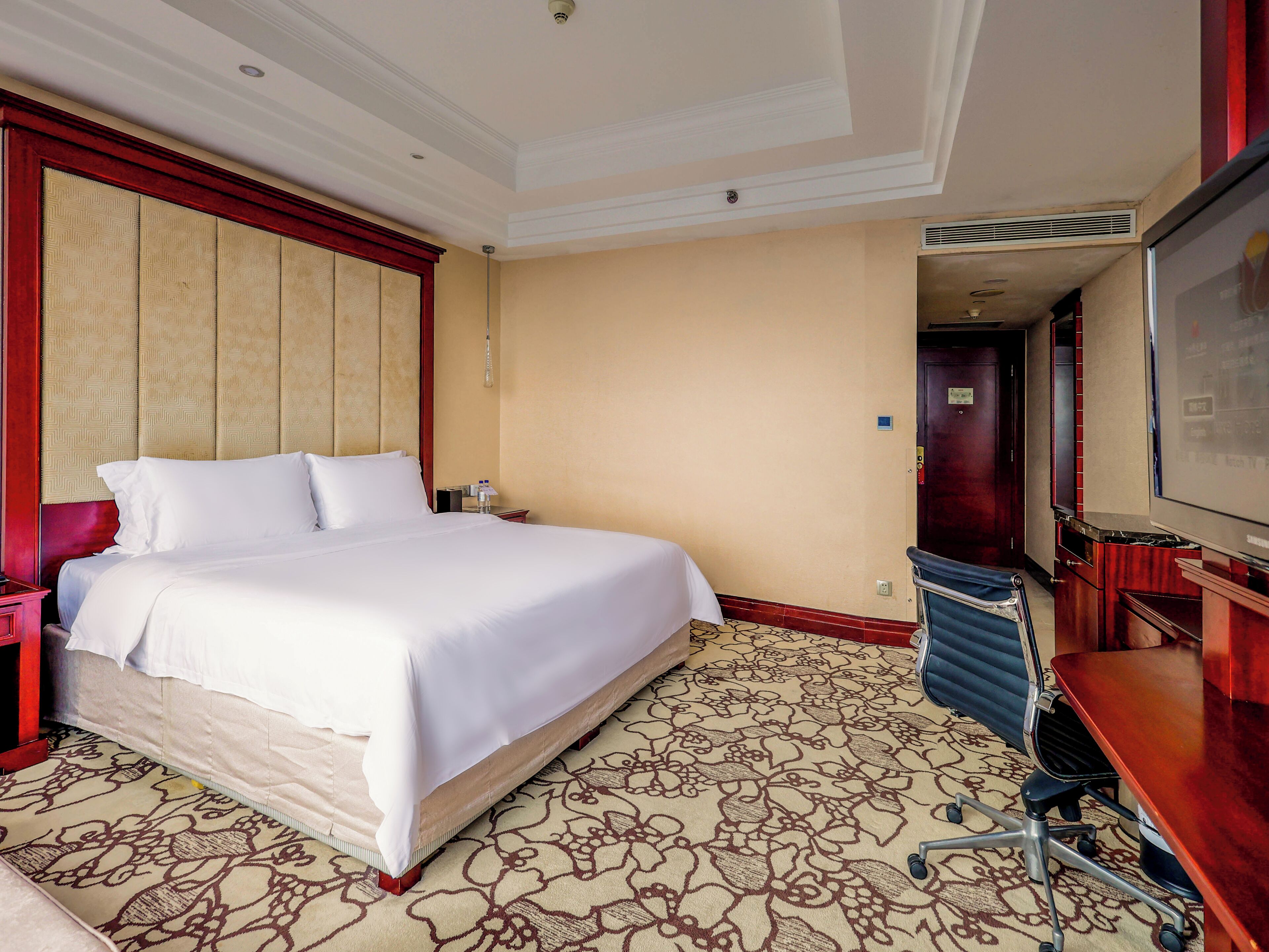 A hotel room with a large bed, a desk with a chair, and a television.
