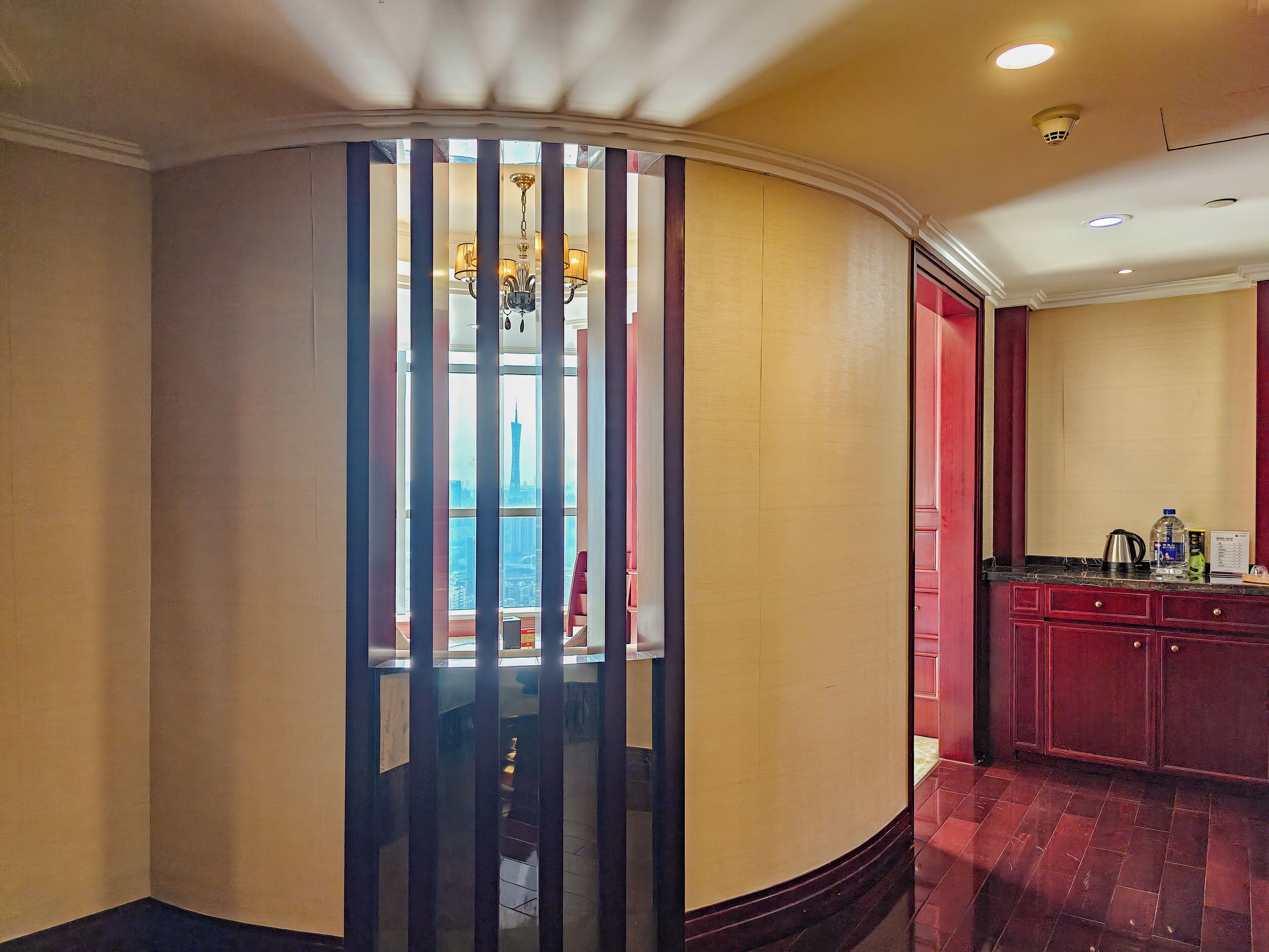 A hotel room with a view of a cityscape, a minibar, and a red cabinet.