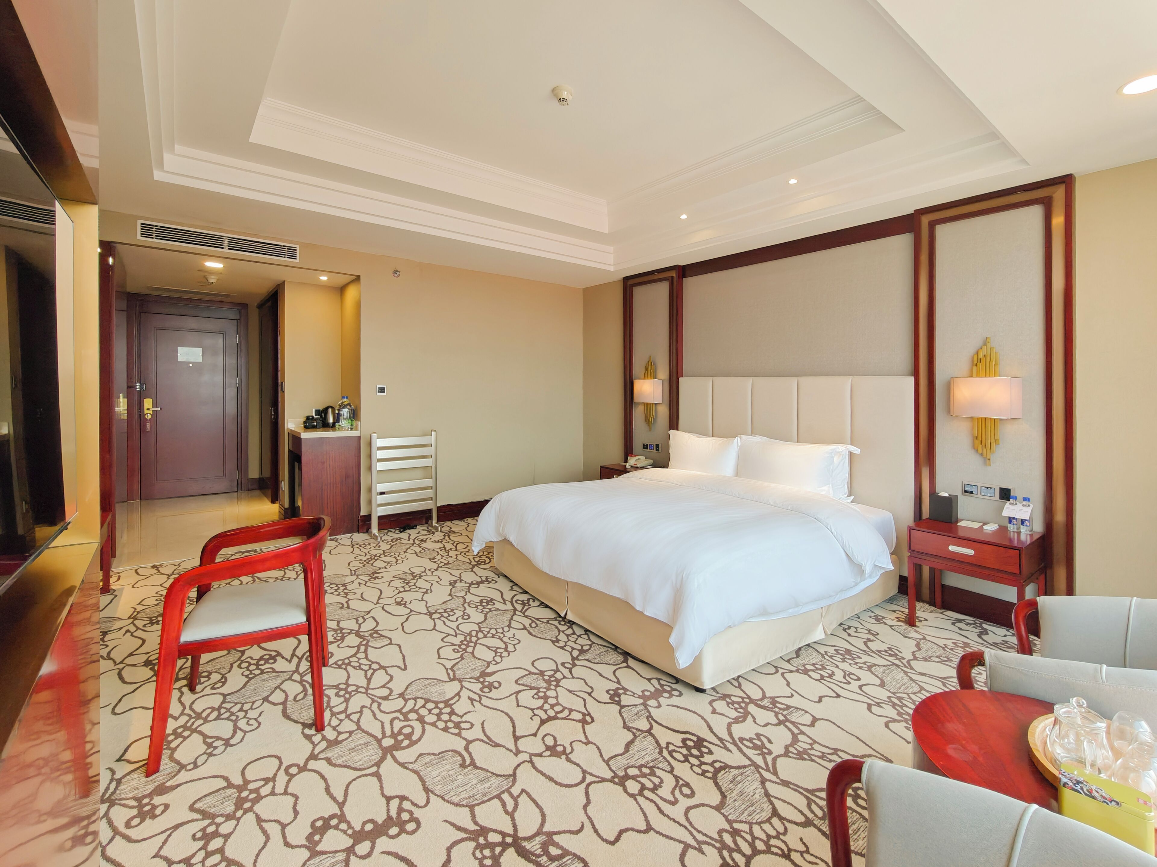 Ein Hotelzimmer mit einem großen Bett, einem Schreibtisch mit Stuhl, einem Nachttisch mit Lampe und einem Spiegel.