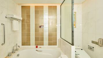 A modern bathroom with a bathtub, toilet, and handrails.