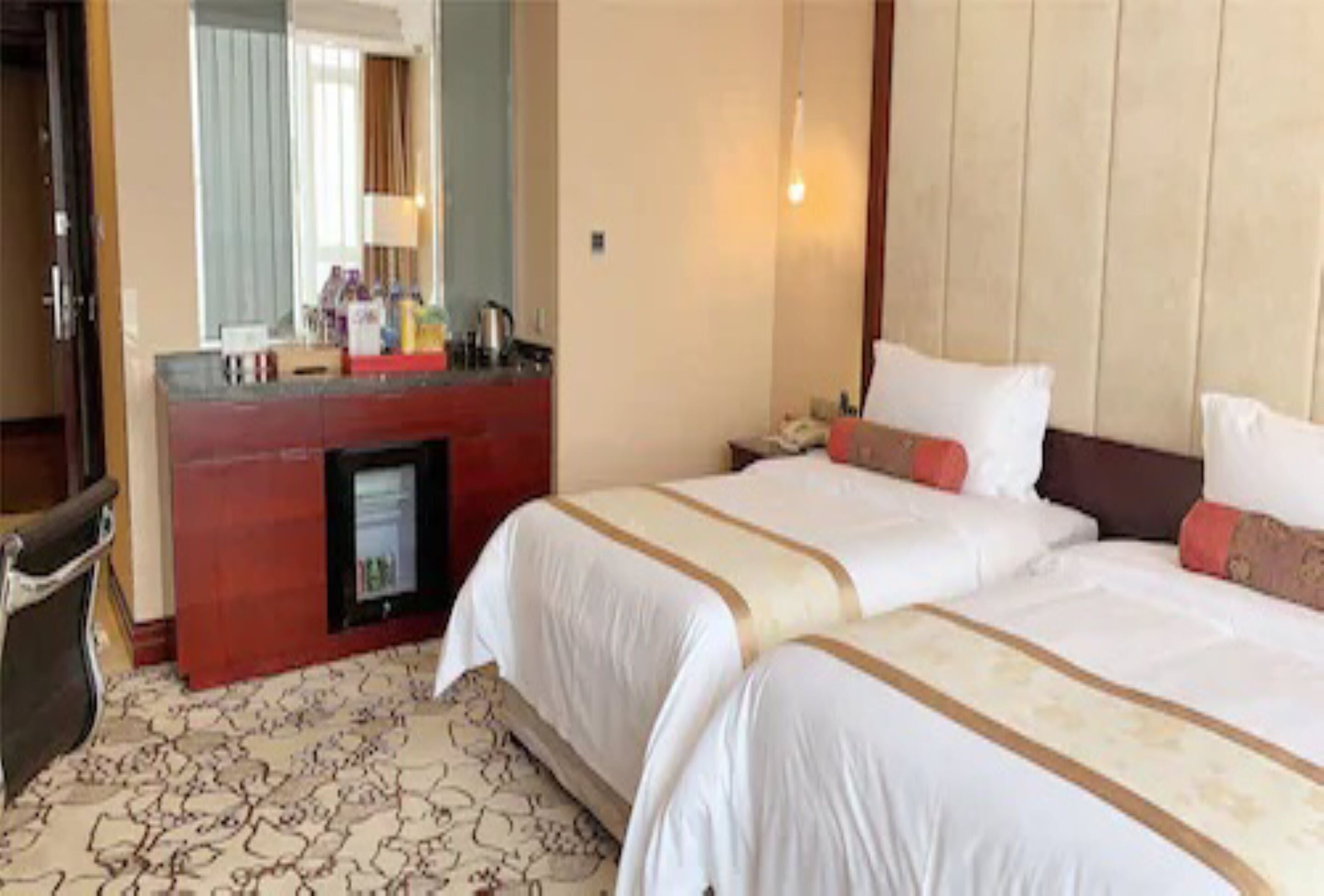 Habitación de hotel con dos camas, un minibar, un escritorio con ordenador y un baño con ducha.
