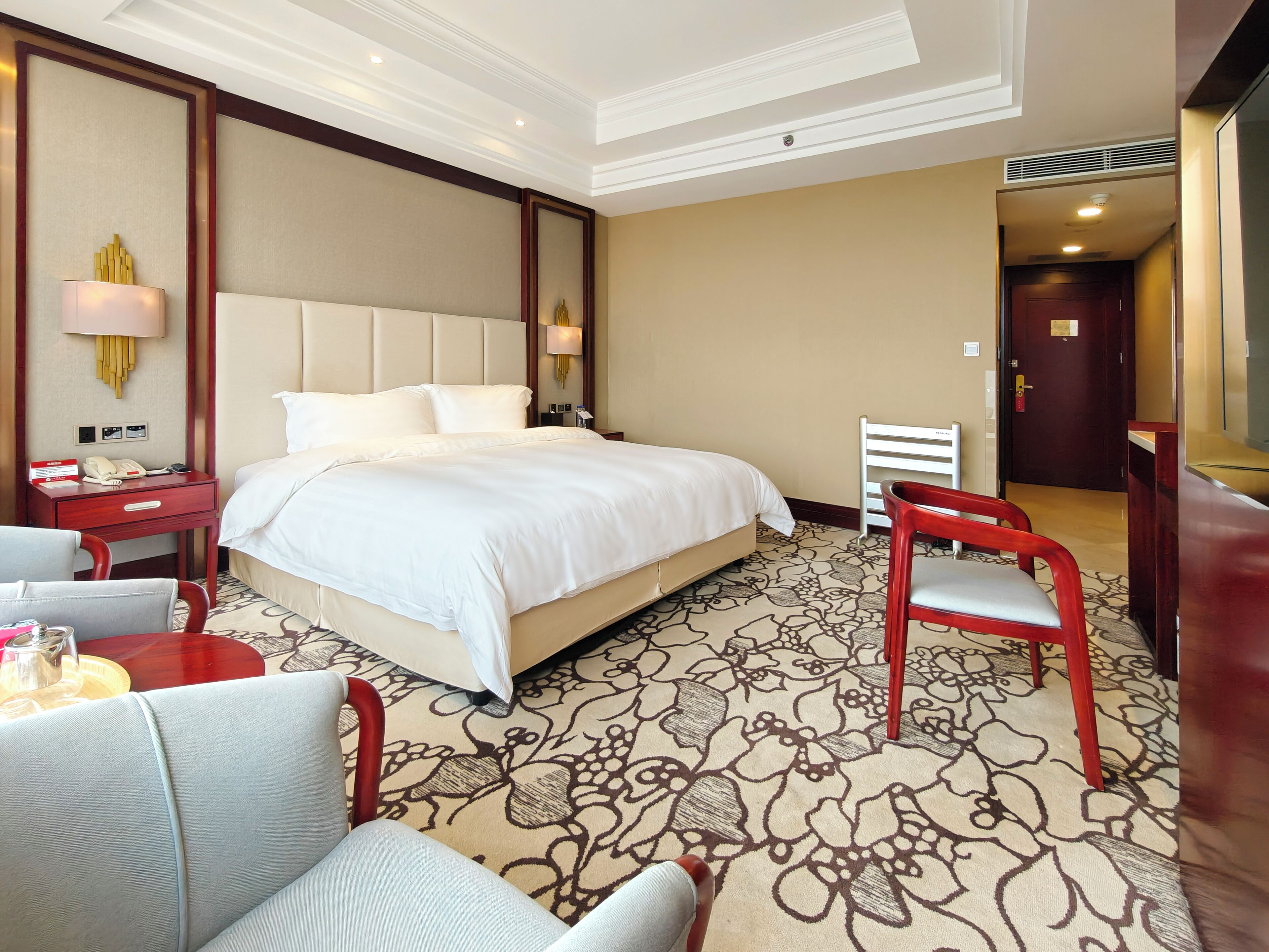 A hotel room with a large bed, a desk with a telephone, a chair, and a TV.