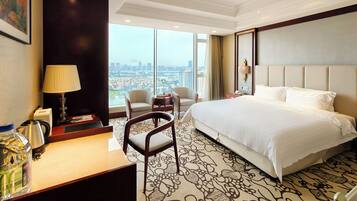 Une chambre d’hôtel avec un grand lit, deux fauteuils, un bureau avec une lampe et une vue sur la ville.