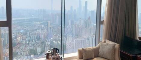 A high-rise room with a city view, a sofa, a small table with a teapot, and a television.