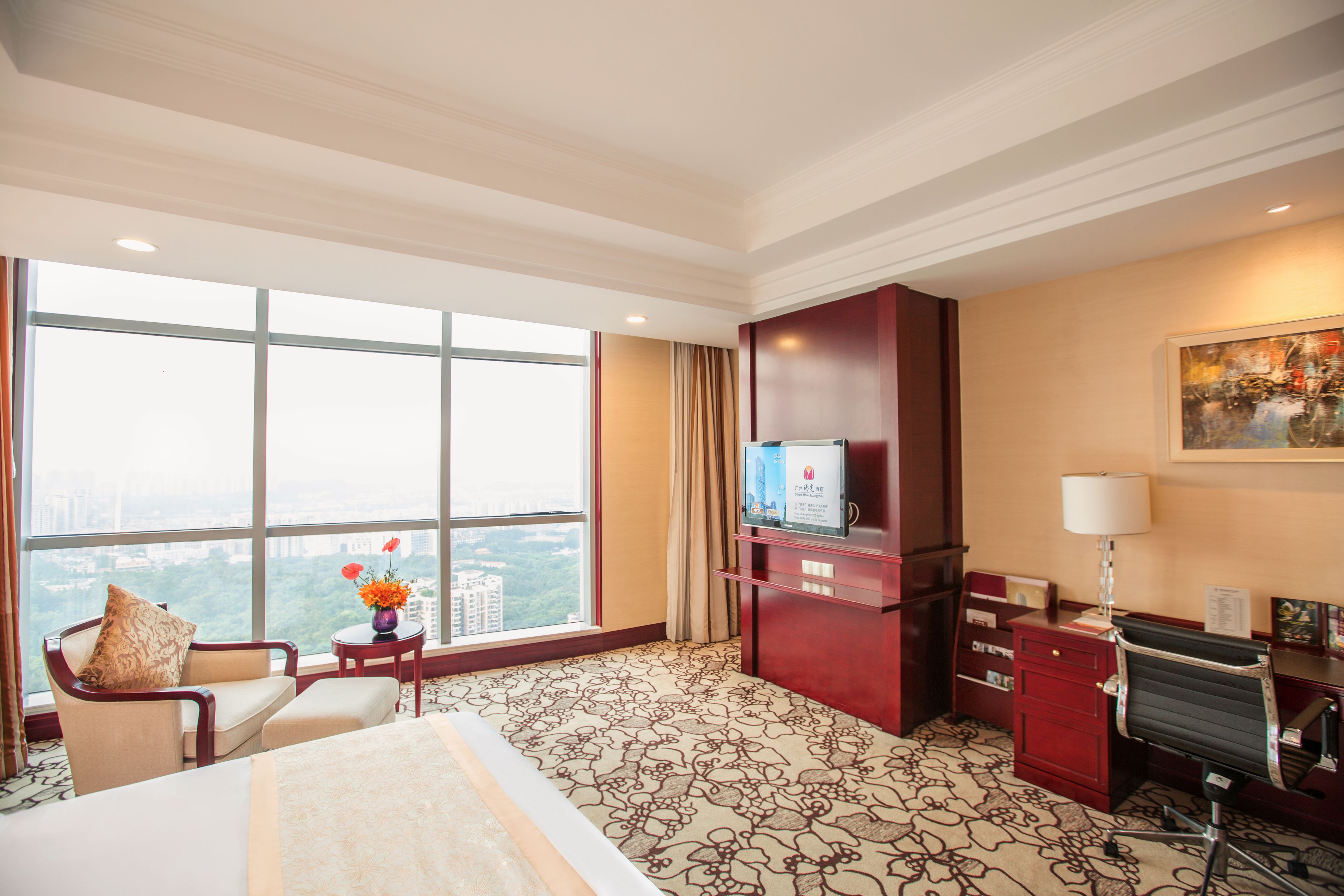 A hotel room with a large window, a bed, a desk, and a chair.
