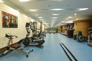 Un gimnasio con máquinas de cardio, bancos de pesas y un espejo grande en la pared.