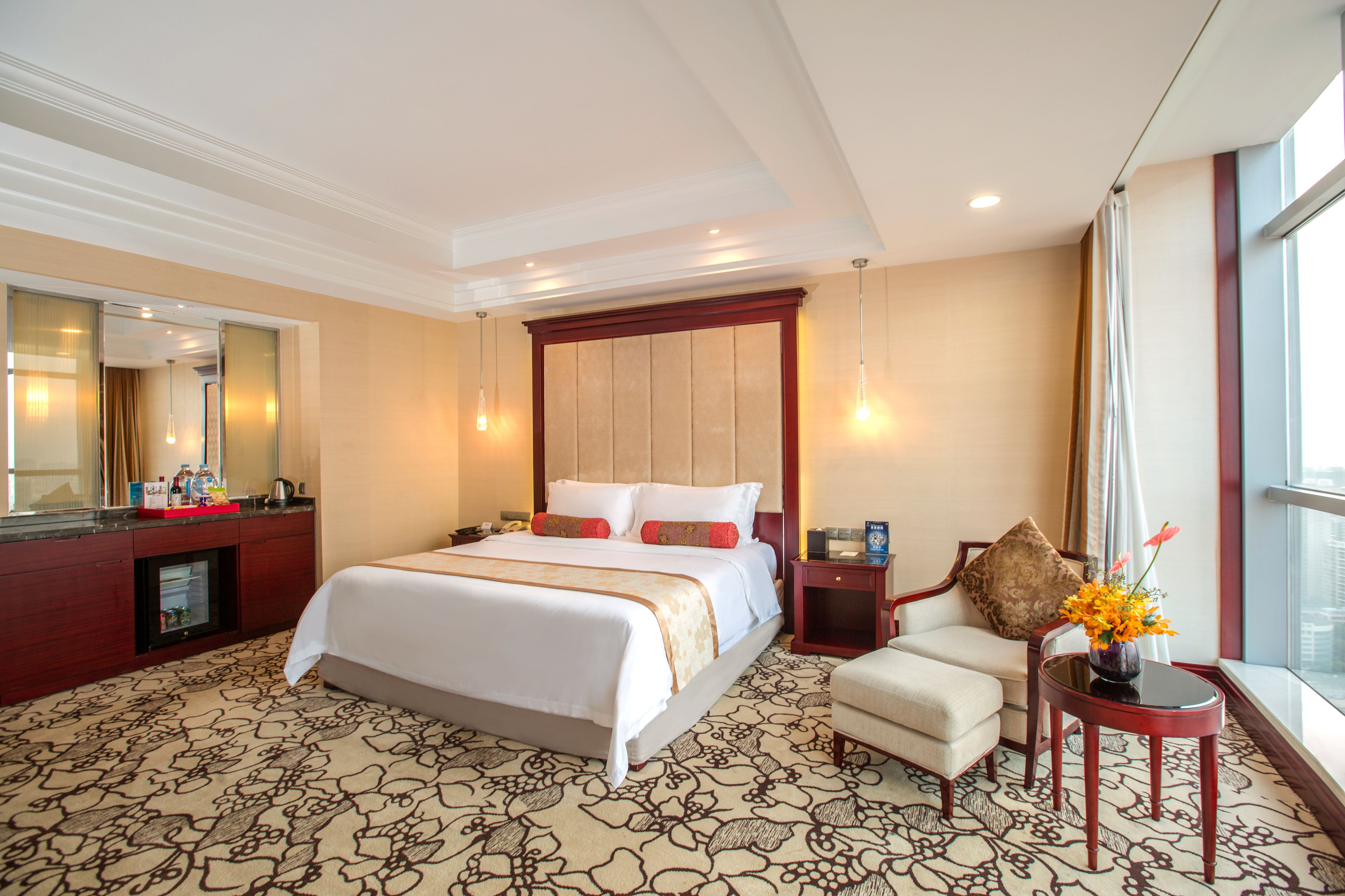 A hotel room with a large bed, a sitting area with a chair and a small table, a mirror, and a window with a view.