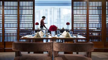 A dining area with a table set for two, a person in the background, and a view through a wooden lattice partition.