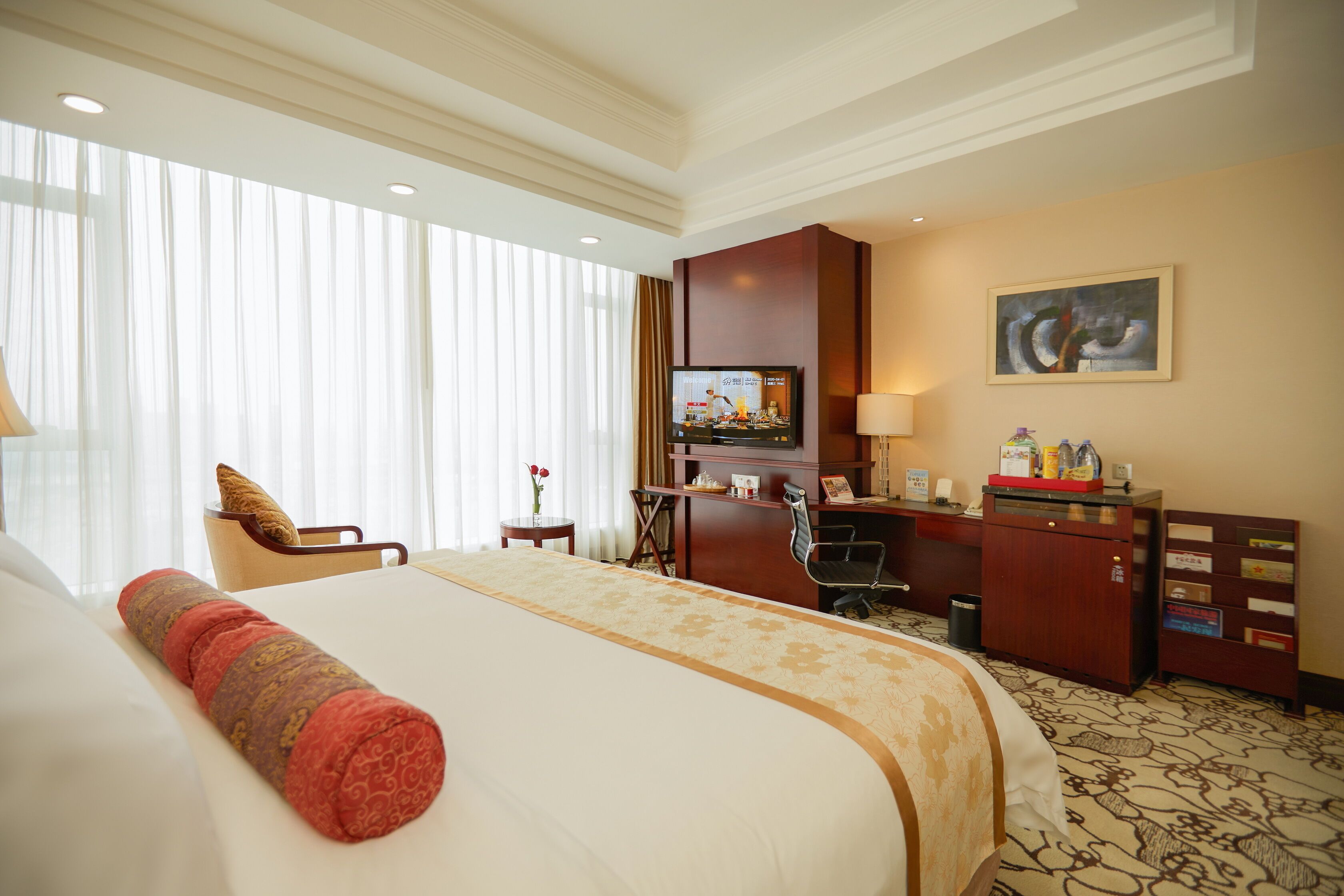 A hotel room with a large bed, a desk, a chair, a television, and a painting on the wall.
