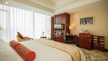A hotel room with a large bed, a desk, a chair, a television, and a painting on the wall.