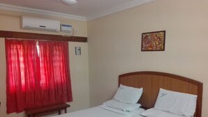 A hotel room with a bed, red curtains, an air conditioning unit, a wall-mounted artwork, and a bedside table. - KTDC Nandanam Guruvayoor (Chavakkad)