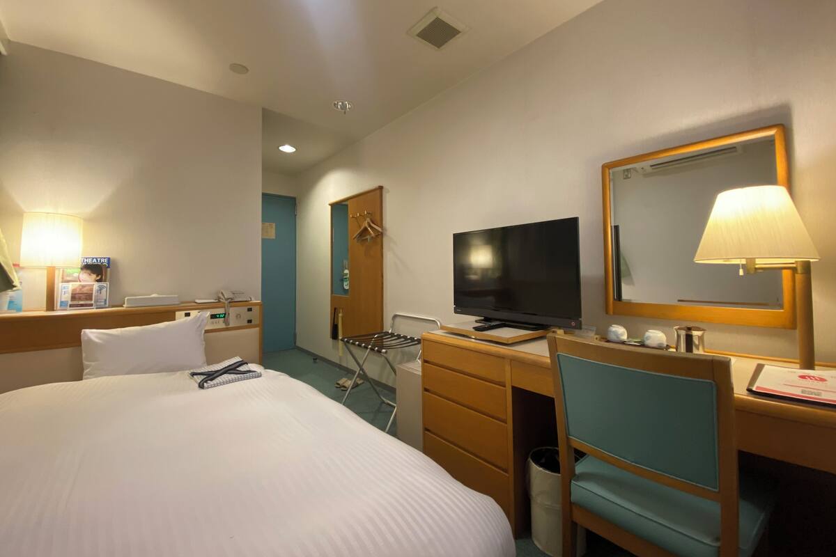 A hotel room with a large bed, a desk with a television, a mirror, and a lamp.