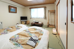 Una habitación de hotel con una cama, televisión, una mesa con hervidor y un futón.