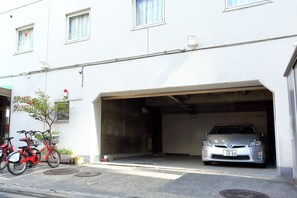 Um edifício com uma garagem, um carro prateado lá dentro e duas bicicletas estacionadas na frente.
