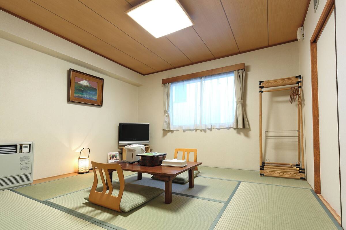 A traditional Japanese room with tatami flooring, a television, a futon bed, and a wooden shelf.