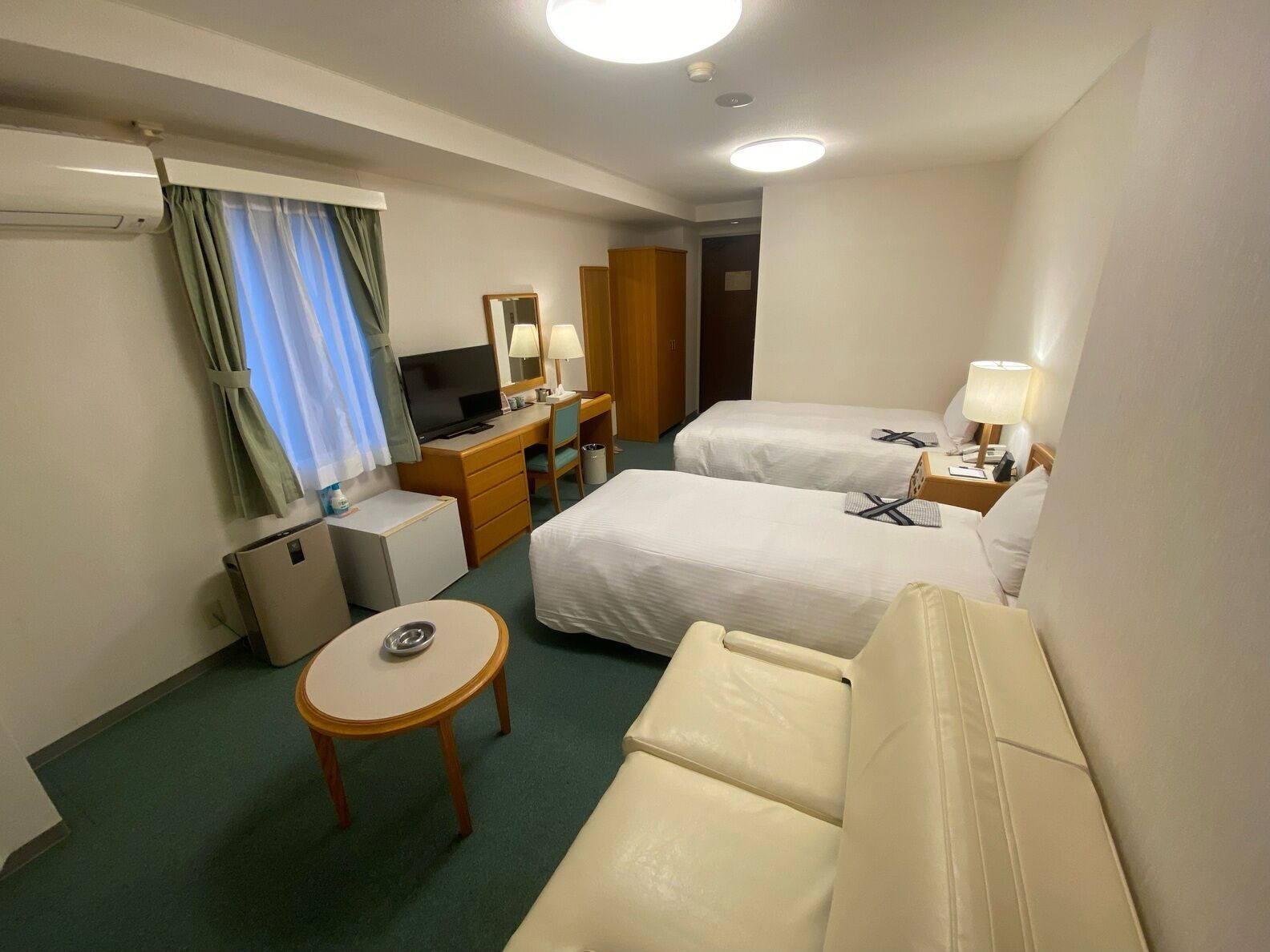 A hotel room with two beds, a desk, a TV, a small table, and a chair.