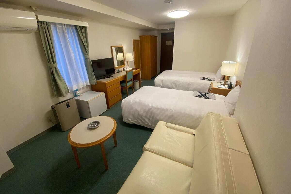 A hotel room with two beds, a desk, a TV, a small table, and a chair.