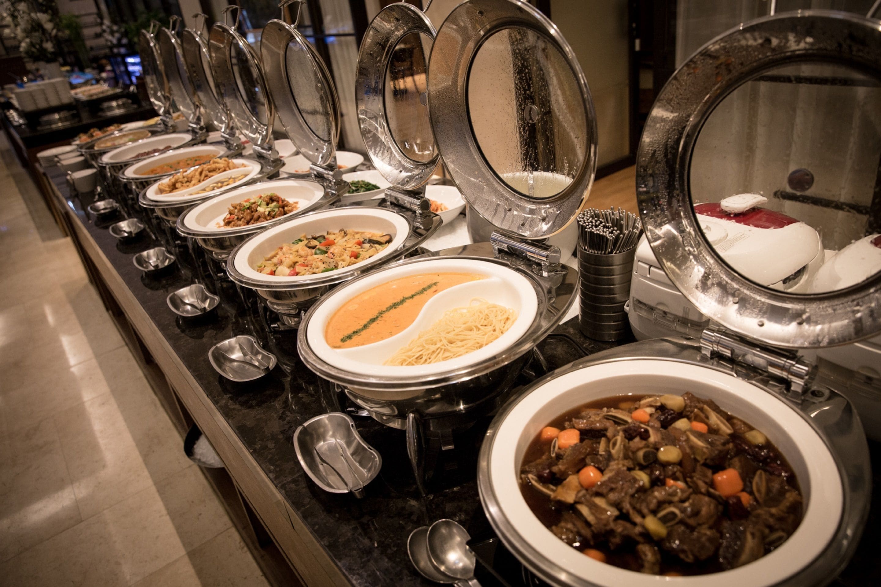 A buffet line with various dishes and utensils.