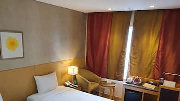 A hotel room with two beds, a desk, a chair, a lamp, a small table, a television, and a window with curtains.