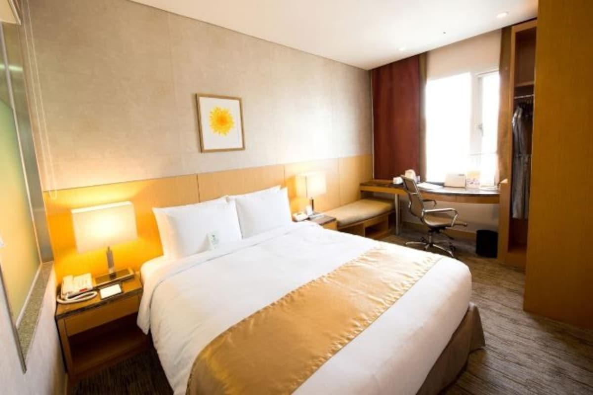 Habitación de hotel con una cama grande, lámparas de noche, un escritorio con silla y una ventana con cortinas.