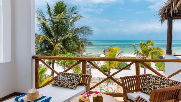 A wooden deck with a view of the beach, a round table with two vases, and a bench with patterned cushions. - Next Paradise Boutique Resort (Pwani Mchangani)