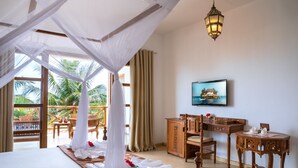A room with a bed, a desk, a chair, a small table, a TV, and a balcony with a view of palm trees. - Next Paradise Boutique Resort (Pwani Mchangani)