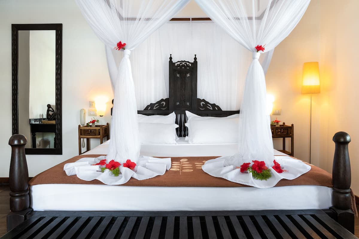 A neatly made bed with a brown bedspread, white pillows, and a canopy with red flowers.