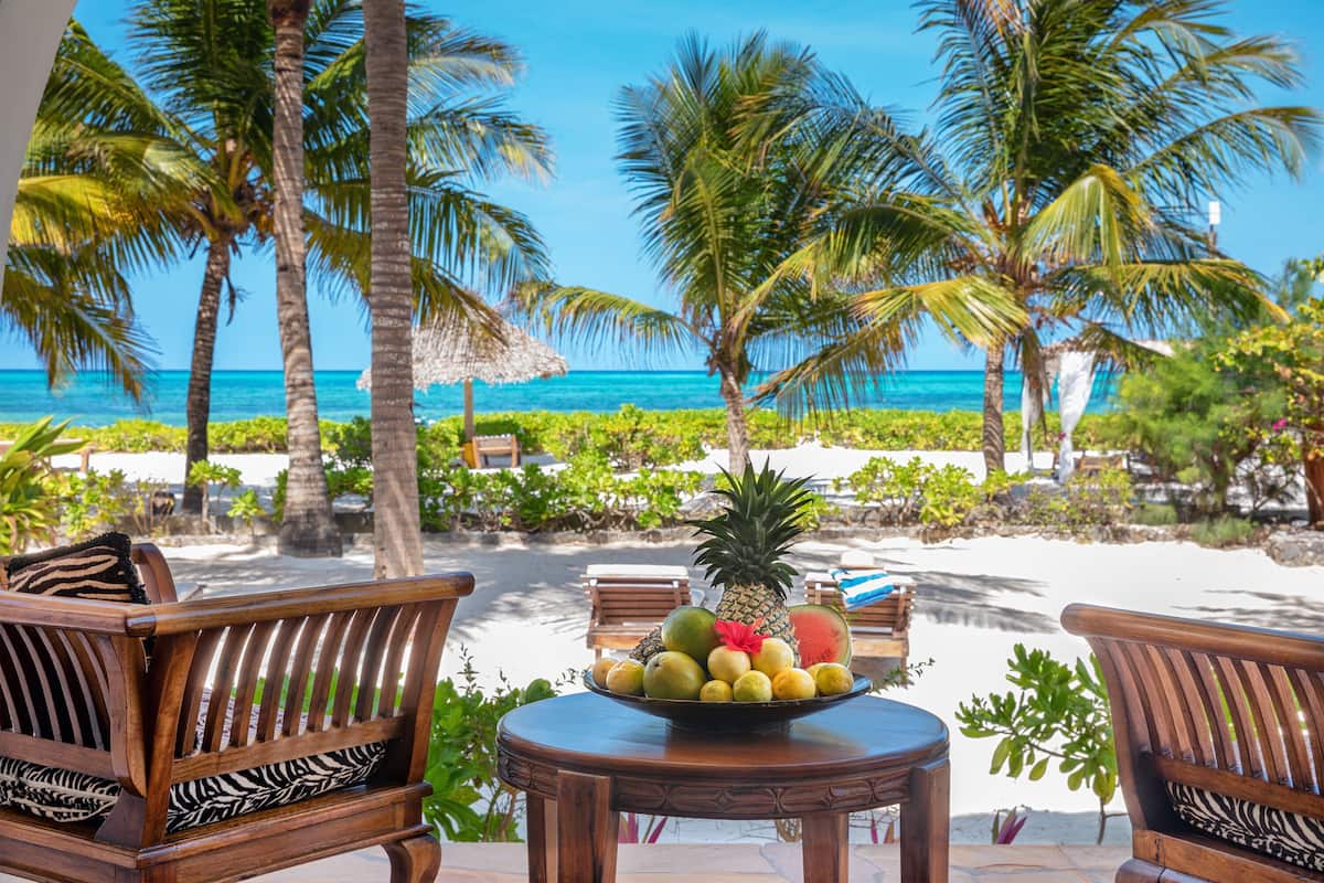 A wooden bench with a fruit bowl in the center, surrounded by palm trees and a view of the ocean.