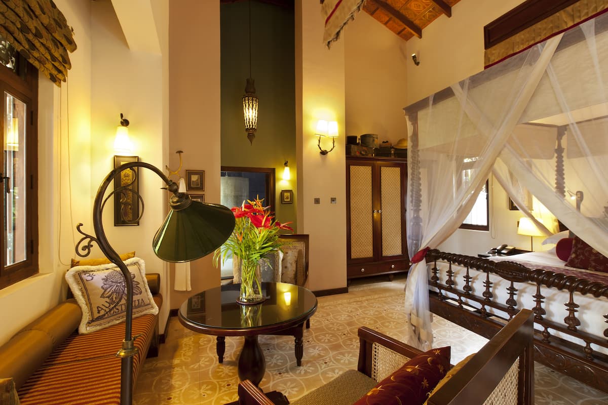 A room with a bed, a table with a vase of flowers, a sofa, and a lamp.