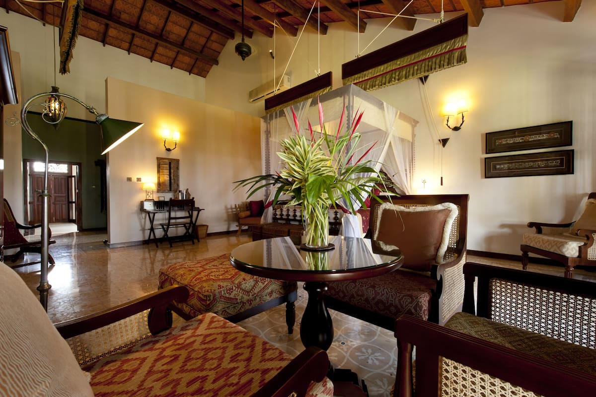 A traditional room with a round table, patterned chairs, a potted plant, and a wooden ceiling.