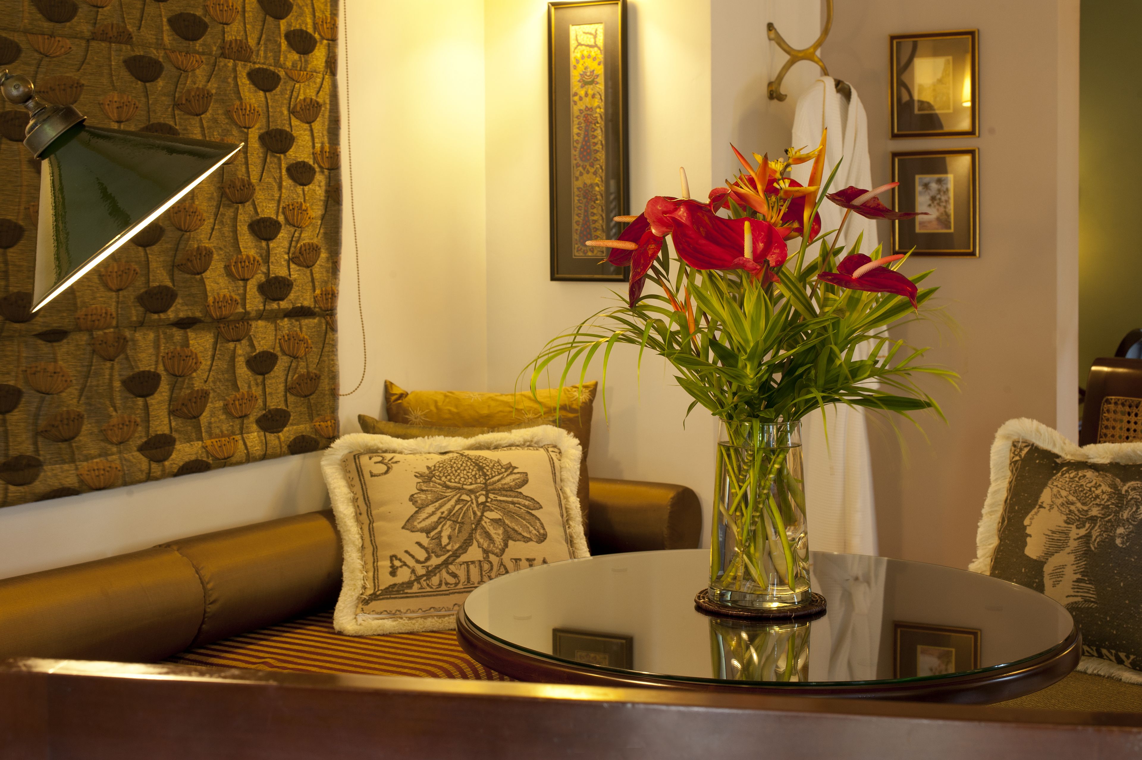 A living room with a round glass table, a vase with flowers, patterned cushions, and framed artwork on the wall.