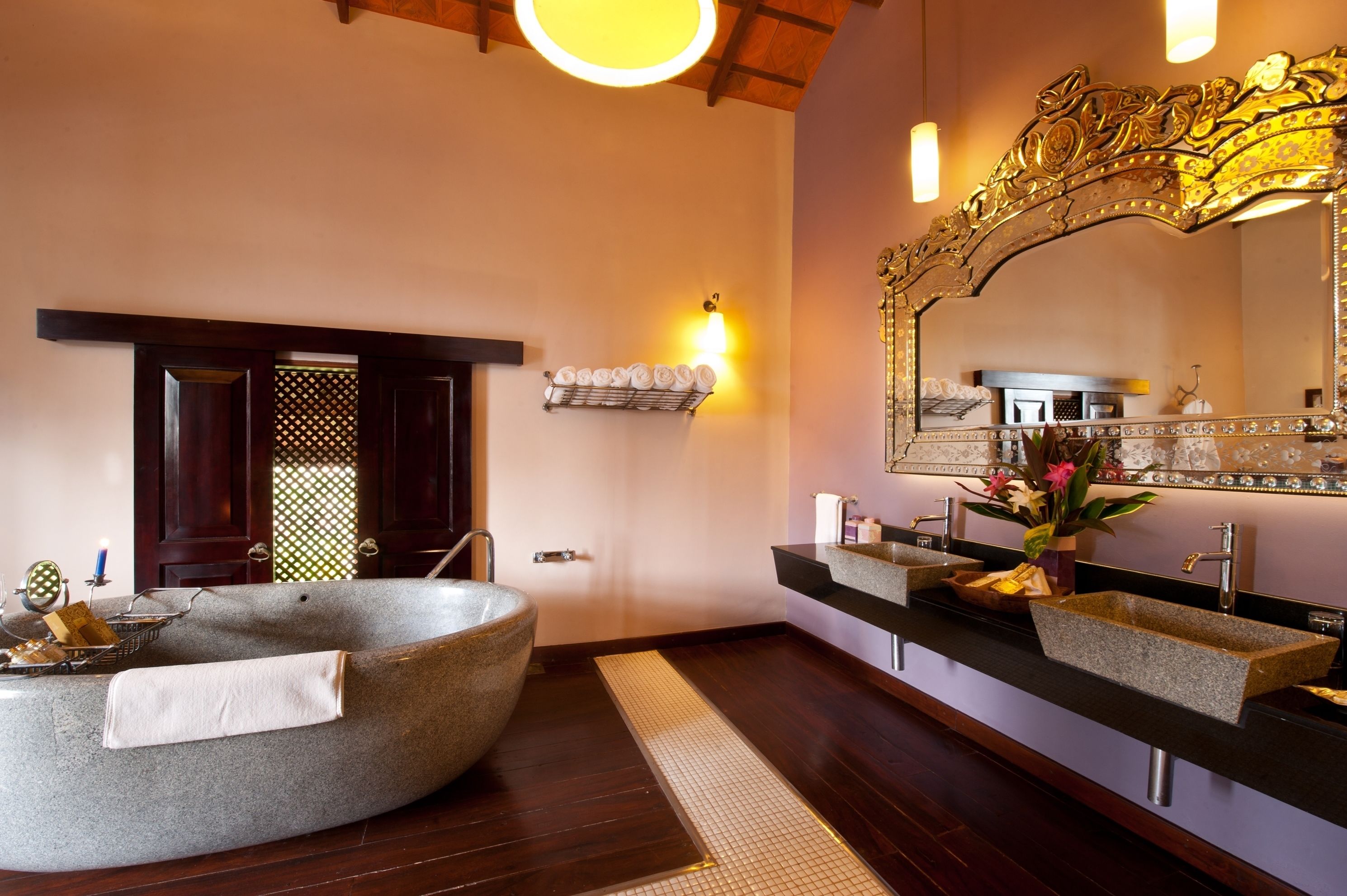 A modern bathroom with a large freestanding bathtub, two sinks with granite countertops, a decorative mirror, and a wooden door.