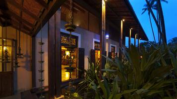 A traditional building with a wooden facade, a hanging water feature, and a view of palm trees.