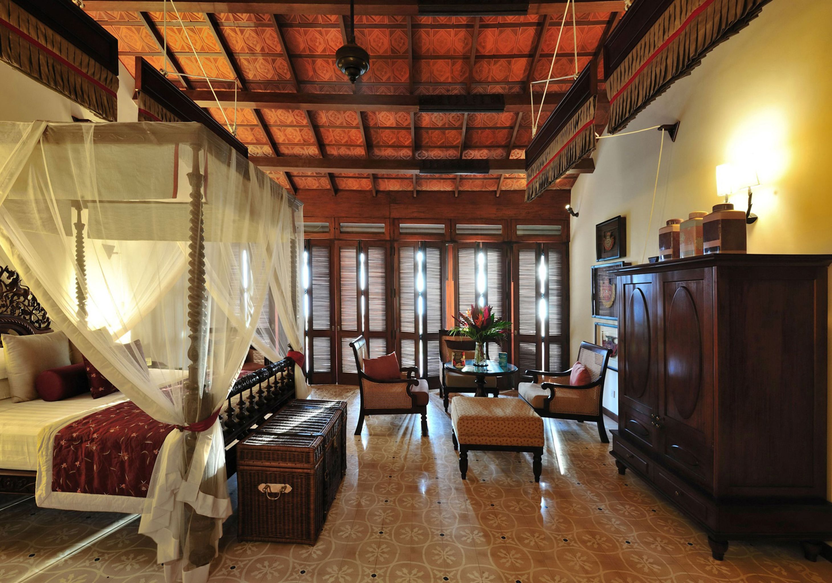 A traditional room with a four-poster bed, a wooden cabinet, and a dining area with chairs and a table.