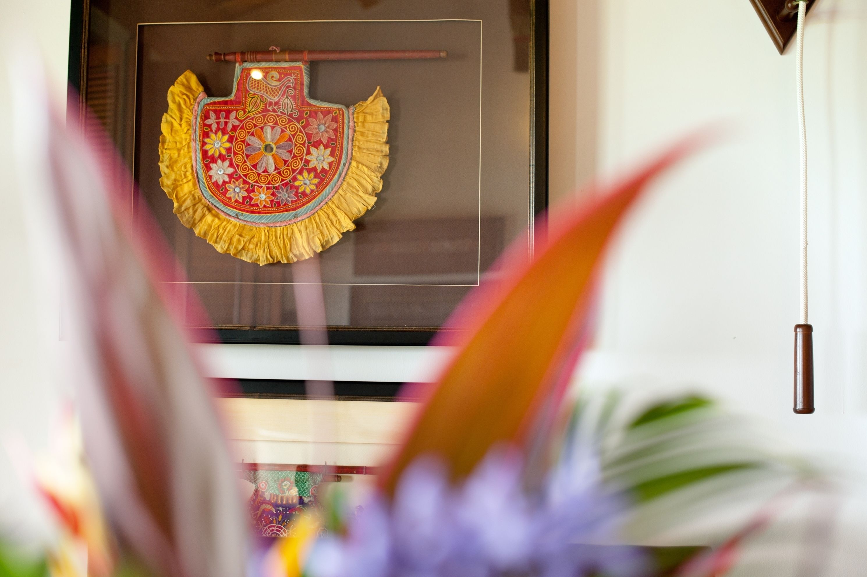 A framed decorative item with a floral pattern and a tassel, displayed on a wall.