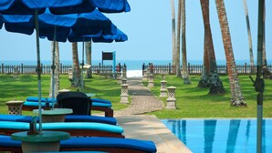 Un área junto a la piscina con sombrillas azules, sillas de descanso y un camino que lleva a la playa.