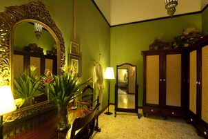 Una habitación con un espejo grande y decorativo, un armario de madera, una lámpara y un jarrón con flores.