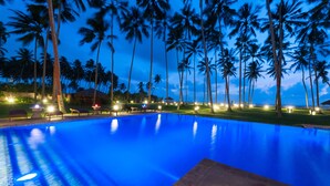 Una piscina con superficie de agua azul cristalina, rodeada de palmeras y zonas de descanso bien iluminadas.