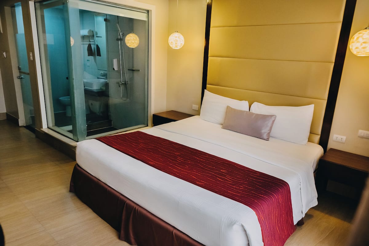 A hotel room with a large bed, a glass shower enclosure, and a bedside table.
