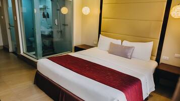 Una habitación de hotel con una cama grande, cabina de ducha de vidrio y una mesita de noche.