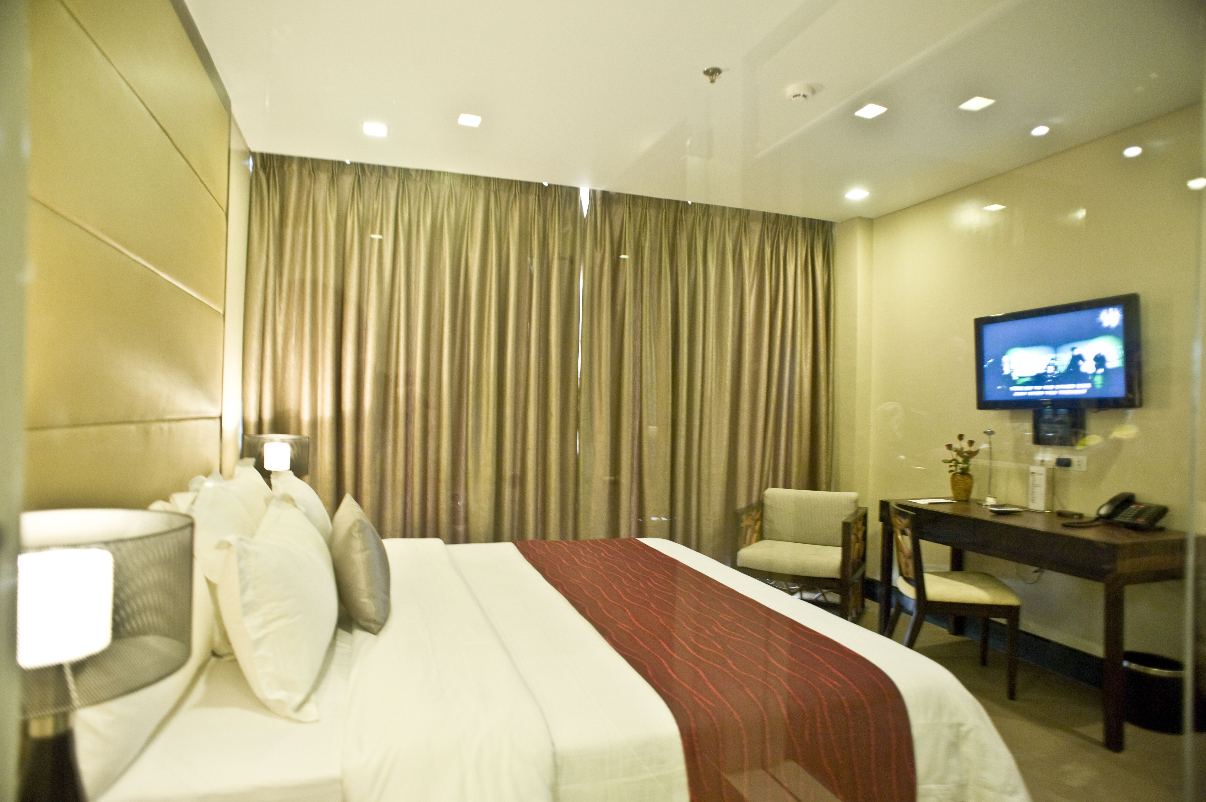 A hotel room with a bed, a desk, a chair, a television, and a curtain.