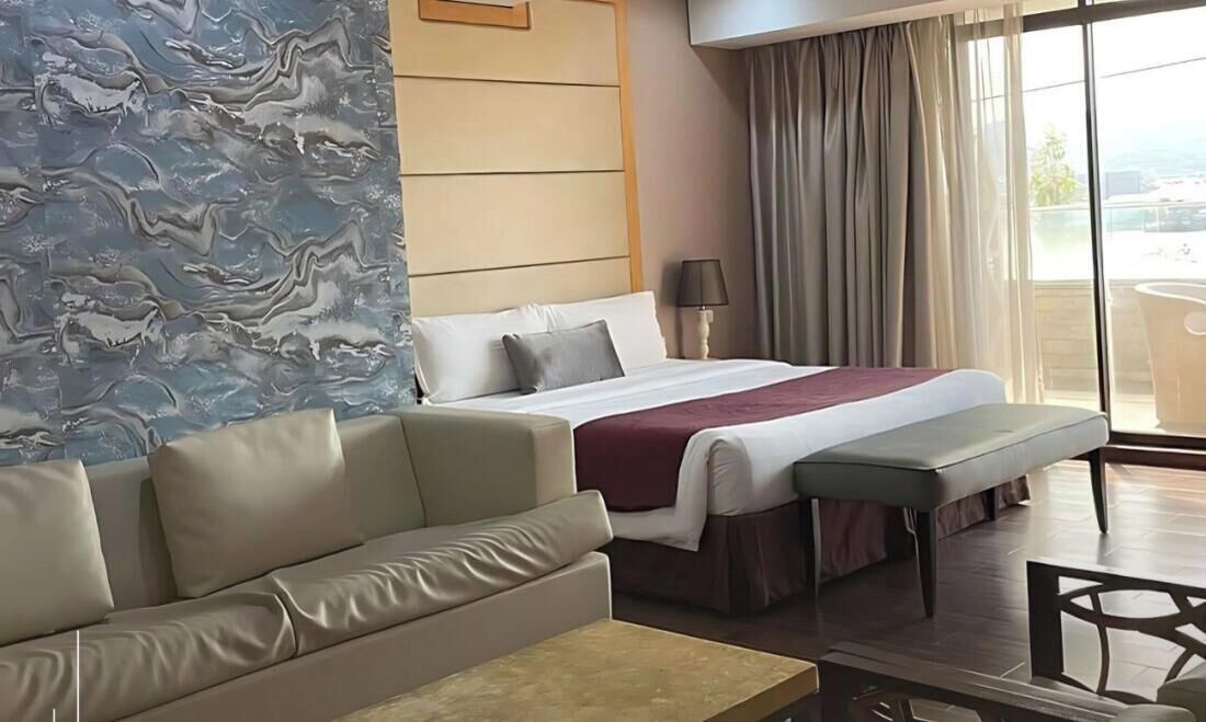 A suite room with a bed, a sofa, a dining table, and a view of the balcony.
