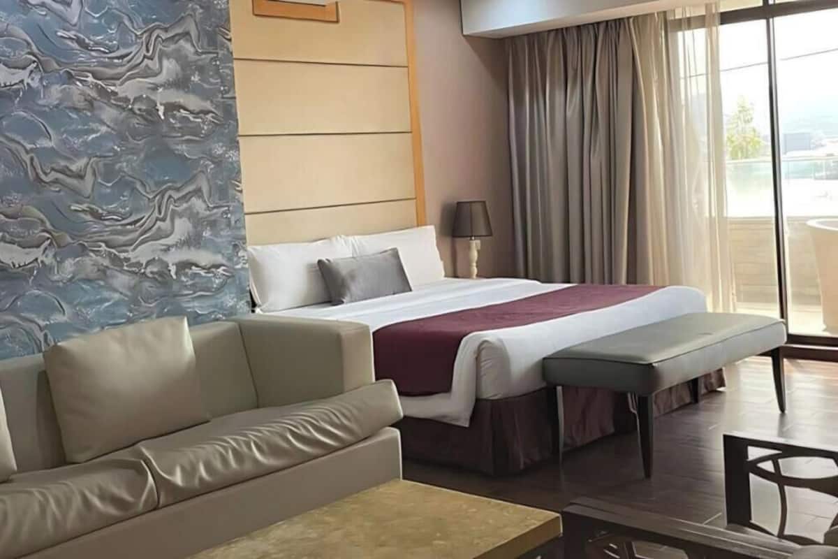 A suite room with a bed, a sofa, a dining table, and a view of the balcony.