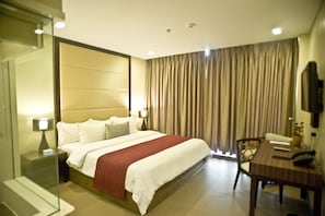 A hotel room with a bed, bedside tables, a desk, a chair, a television, and a window with curtains. - Goldberry Suites & Hotel Mactan (Lapu-Lapu)